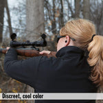 A woman with blonde hair in a ponytail aims a rifle, wearing a black earplug in her right ear.