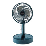 A young girl smiles while sitting at a desk with a dark green portable fan blowing cool air.