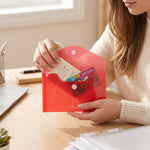 A person's hands are shown opening a translucent red plastic folder, revealing a gift card and other small papers inside.