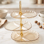 An empty three-tier amber acrylic serving stand with scalloped edges sits on a white marble surface.