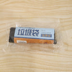 A clear plastic-wrapped roll of black garbage bags with a blue and brown label on a wooden surface.