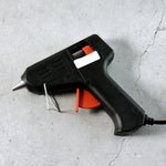 A black and red glue gun with a white label and a metal stand, resting on a gray concrete surface.
