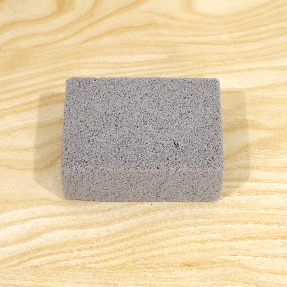 A single gray rectangular cleaning block with a porous texture centered on a light wooden surface.
