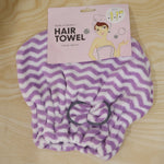 A purple and white chevron microfiber hair towel with a grey bow, displayed with its pink packaging on wood.
