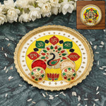 A yellow and gold puja thali with peacock design, small bowls of red powder and rice, with white flowers in the background.