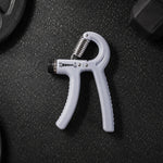 A gray adjustable grip strength trainer with a metal spring lies on a dark gym floor next to a weight plate.