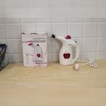 A white and pink handheld steamer with its packaging box, both featuring an apple logo, on a wooden surface.