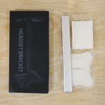 Disassembled silver and white headphone stand components in clear plastic packaging next to its black box.
