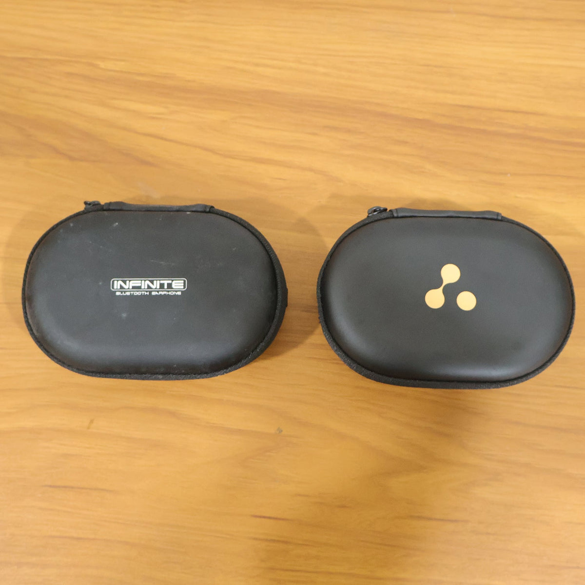 A black oval hard shell charging cable and adapter storage case (1 Pc) is shown closed with a gold three-dot logo.