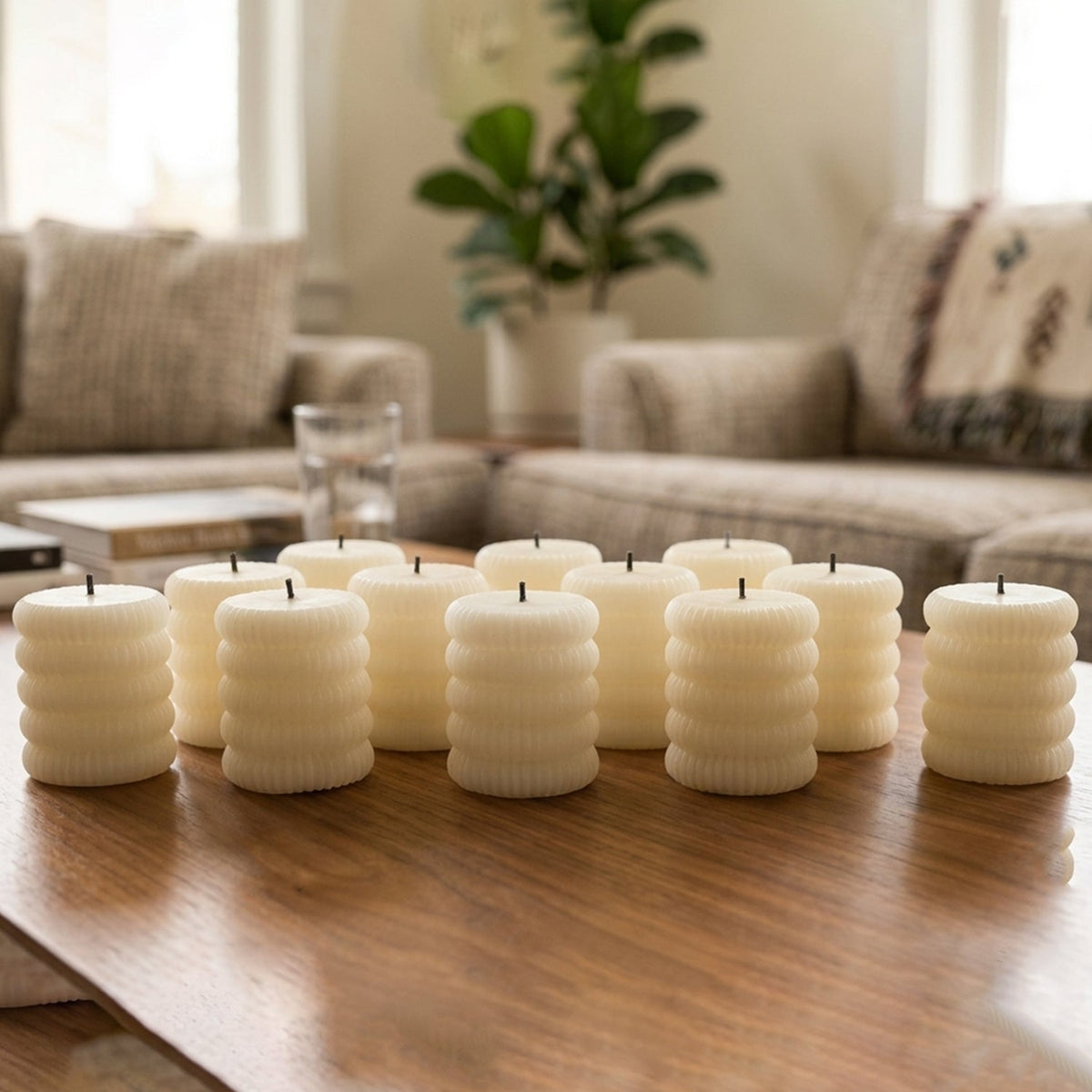 Twelve unlit cream ribbed LED candles are arranged on a wooden table in a bright, modern living space.