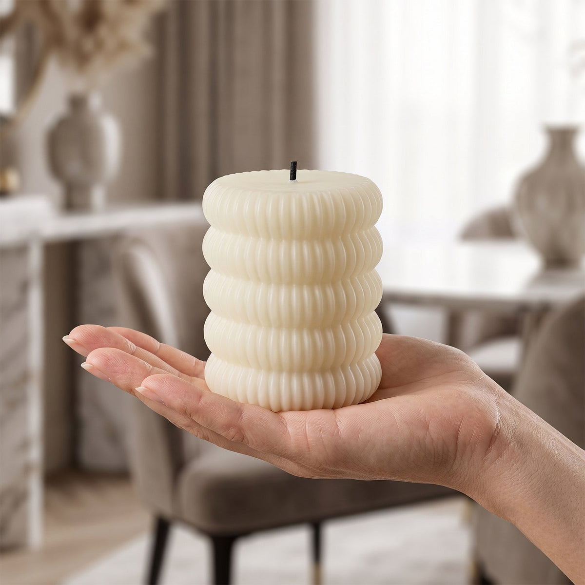 A single cream ribbed LED candle is held in an open palm, with a blurred living room background.