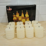 Twelve unlit cream ribbed LED candles are arranged in front of a black product box on a light wooden surface.