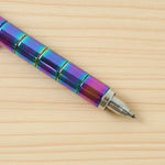 A close-up of the tip of a rainbow-colored magnetic fidget pen on a light wooden surface.