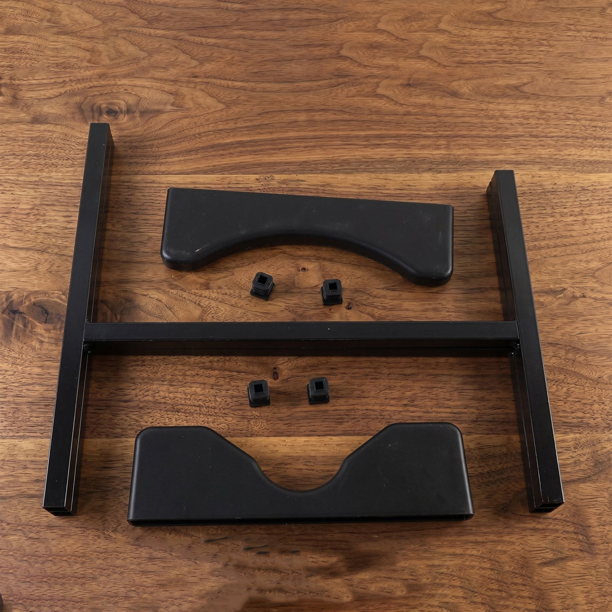 Disassembled black metal water bottle stand components, including two frame pieces, two cradles, and four small caps, lay on