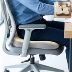 A person sitting on a grey office chair with a beige and grey ergonomic seat cushion