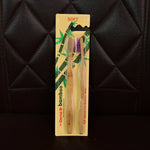 A two-pack of Dental B bamboo toothbrushes, one with brown and one with purple bristles, in yellow packaging against a dark