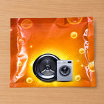 An orange powder sachet with a washing machine drum and miniature washing machine graphic on a wooden surface.