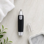 A black and silver nose hair trimmer with its clear cap removed lies on a white marble surface next to a white towel and