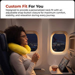 A woman with glasses relaxes on an airplane at night, wearing a yellow neck pillow and looking out the window.
