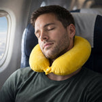 A man rests on an airplane seat, wearing a yellow U-shaped neck pillow with a buttoned closure around his neck.