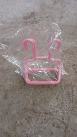 A single pink plastic shoe drying rack is sealed inside a clear plastic bag on a textured grey surface.