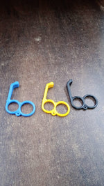 Three plastic finger ring phone holders in blue, yellow, and black are arranged on a dark wooden surface.