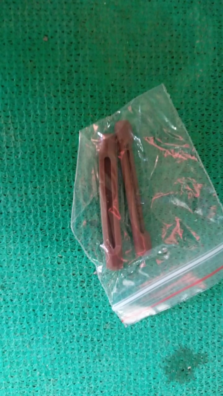 Two brown anti-slip eyeglass ear grips sealed in a clear plastic bag on a green mesh surface.
