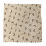 A beige microfiber towel with a dark bow pattern and scalloped edges lies flat on a white background.
