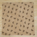 A beige microfiber towel with a dark bow pattern and scalloped edges lies flat on a light wood surface.