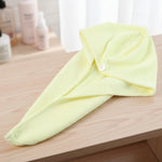 A yellow microfiber hair drying wrap towel with a white button is neatly folded on a light brown wooden surface.