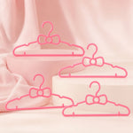 Four pink plastic bow-shaped hangers are arranged on and around two pink display blocks on a pink background.