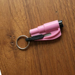 A pink emergency car window breaker and seat belt cutter tool with a black keychain rests on a warm brown wooden surface.