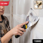 A person uses a 100mm stainless steel putty knife with a black and yellow handle to apply white putty to a wall.