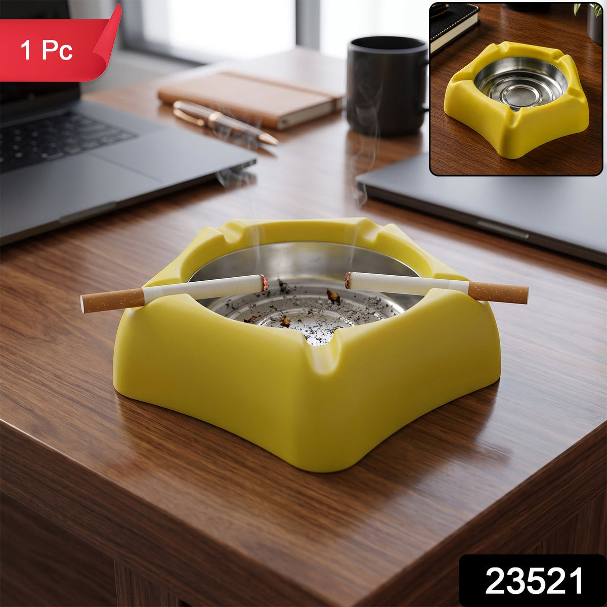 A yellow silicone ashtray with a stainless steel insert, holding two lit cigarettes, sits on a wooden desk with laptops,