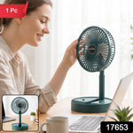 A dark green portable fan with a white USB cable on a wooden desk with a laptop and iced tea.