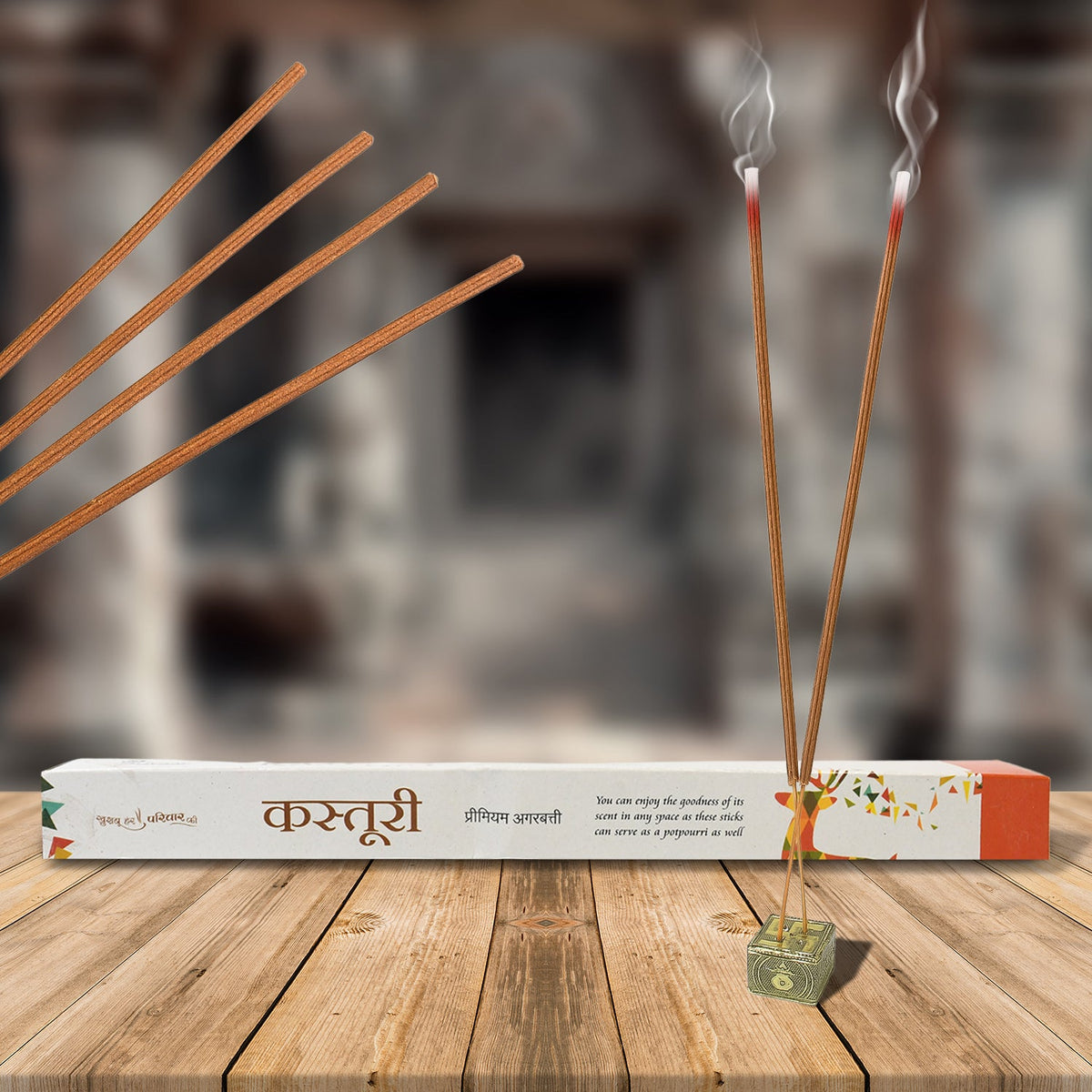 Two burning brown incense sticks in a holder, with a white box and more sticks in the background.