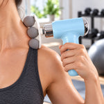 A person uses a light blue massage gun with three grey spherical heads on their shoulder, in a gym setting. – view 4