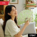A woman in a light dress sits on a sofa, fanning herself with a green plastic fan, with product details overlaid.
