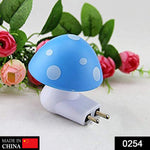 A blue and white mushroom-shaped night light with a two-pin plug is shown against a blurred background of pink flowers.