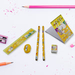 Unicorn-themed pencils, ruler, sharpener, eraser, and notebook on a white surface with pink pencil shavings and a pink