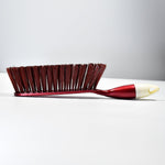 A red and white handled brush with brown bristles is shown from the side on a plain white background.