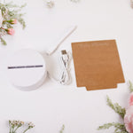 The disassembled lamp components: a white round base, a USB cable, a white marker, and a brown acrylic board, surrounded by