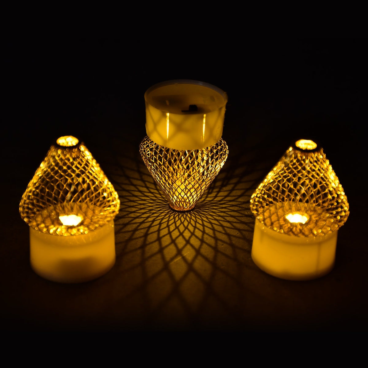 Three golden mesh LED tea lights casting intricate shadow patterns on a dark surface.