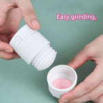 Hands holding a white pill grinder with pink crushed powder in the bottom section.