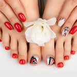 Manicured hands and feet with red and patterned nail polish holding a white flower.
