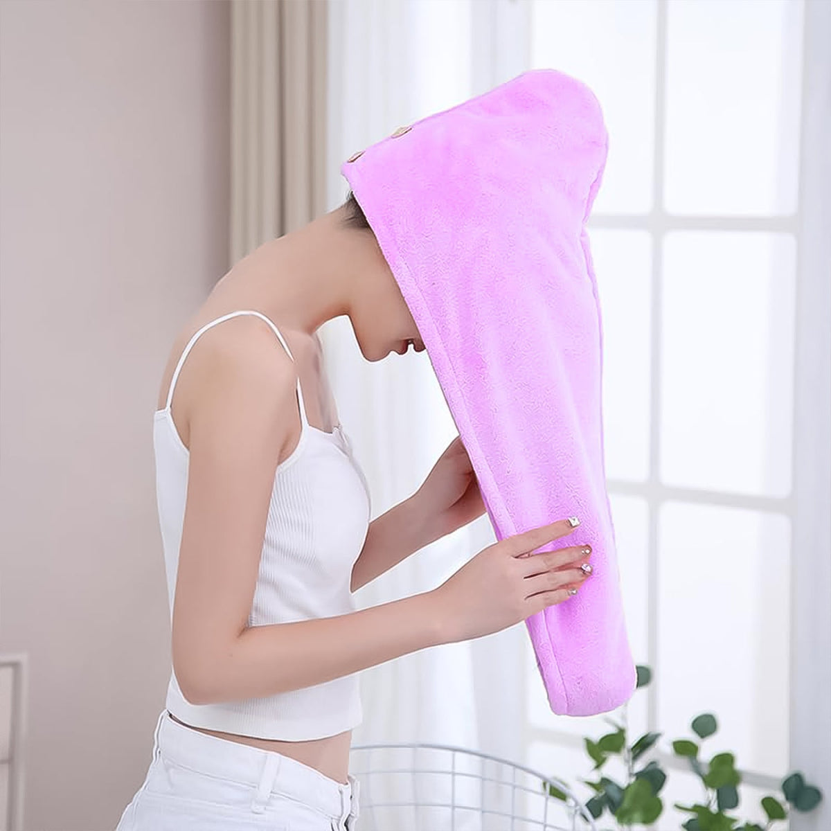 A woman with her head bent forward is about to put on a purple microfiber hair wrap, holding it open.