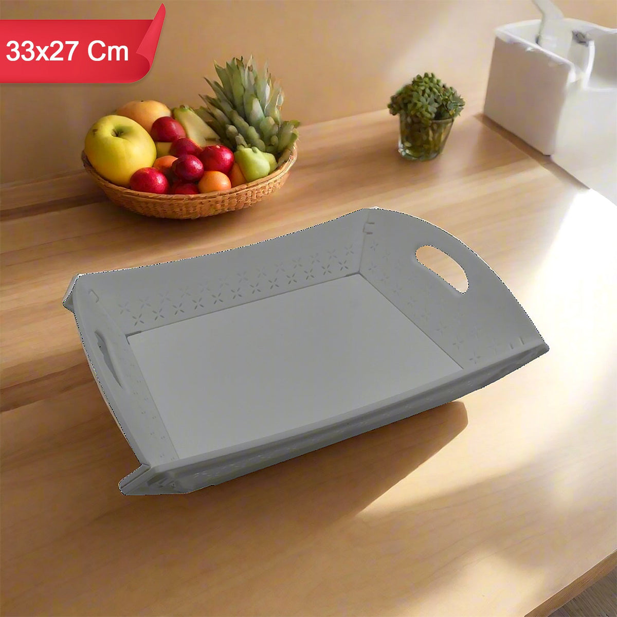 A white foldable serving tray sits on a wooden counter next to a fruit basket and a small plant.