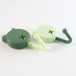 Two cat-shaped wall hooks, one dark green and one light green, lying on a white surface, showing their side profiles.