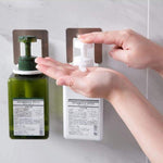 A person dispenses white lotion from a white bottle in a wall-mounted holder, next to a green bottle in another holder.