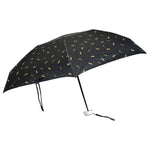 The black compact umbrella is fully open, displaying its gold musical note pattern against a white background.